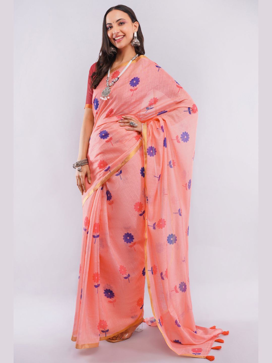 Peach linen saree with purple and red daisy floral prints and gold zari border draped by woman for summer wear by Samantha